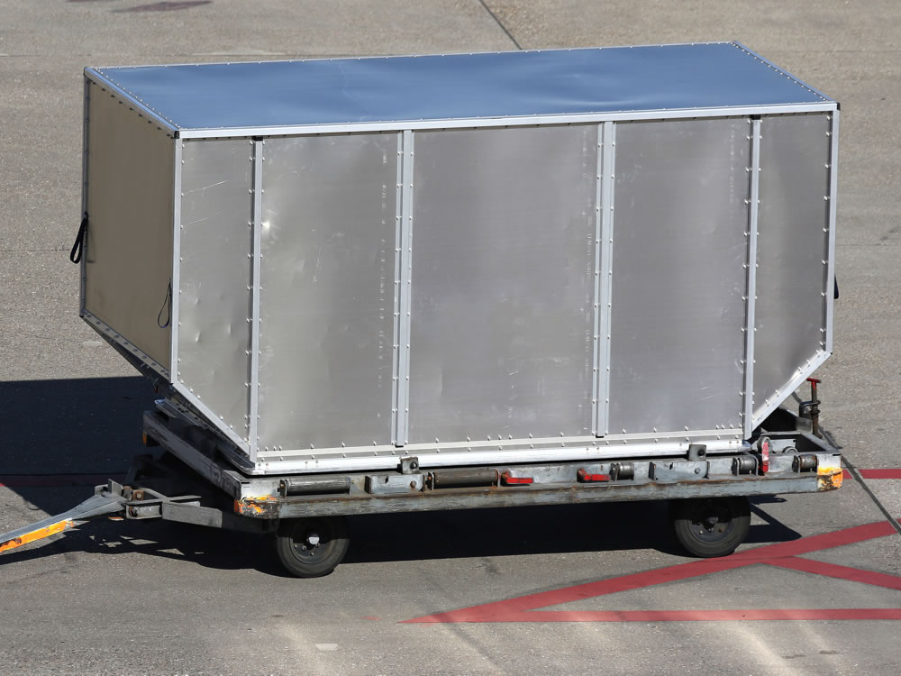 Contêiner metálico para transporte aéreo sendo movimentado na pista de um aeroporto.