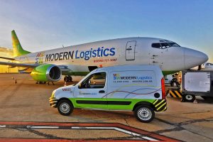 Avião Boeing 737-300F da Modern Logistics e van de apoio logístico estacionados em aeroporto durante operação de carga.